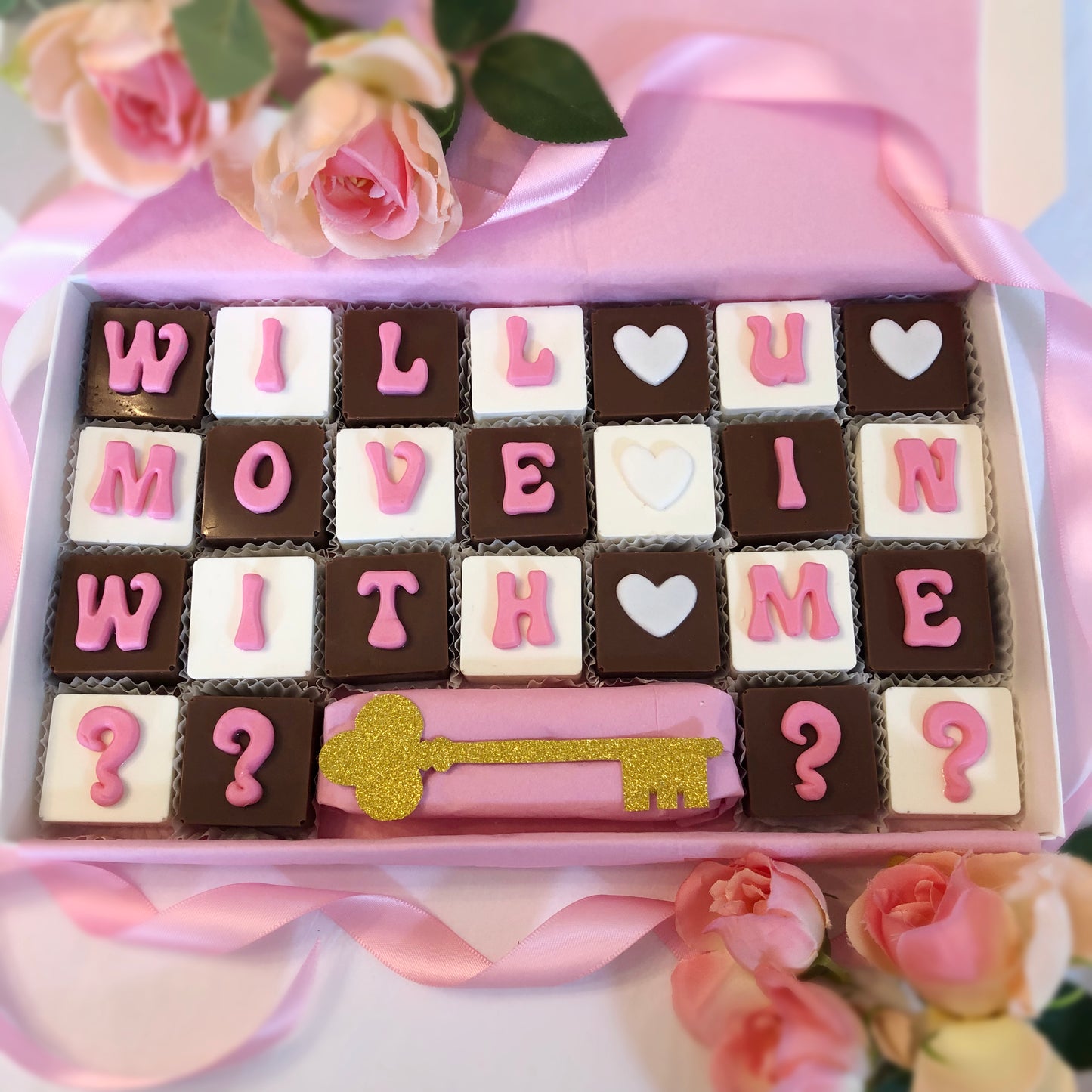 Solid square chocolates with one fondant letter on each, spell out - Will you move in with me ???? and offers a gold sparkle key.