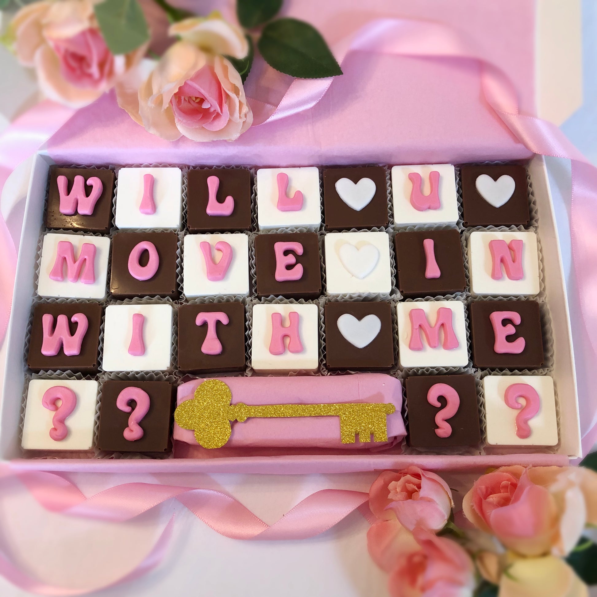 Solid square chocolates with one fondant letter on each, spell out - Will you move in with me ???? and offers a gold sparkle key.